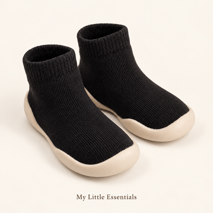 Black sock shoes with cream soles on an ivory background